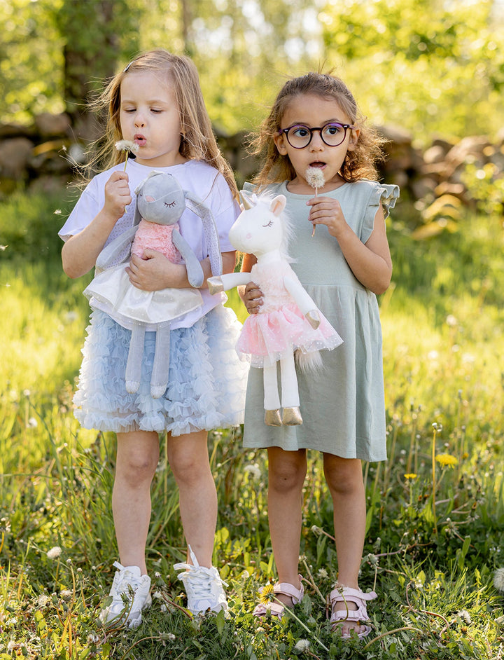 Two young girls standing in a grassy field holding stuffed animals.