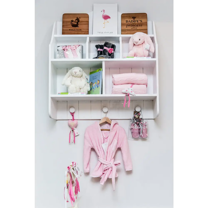 White Lyra wall shelf with open cubbies, pigeon holes, tongue-and-groove detail and three rounded hooks, styled for nursery or kids’ room
