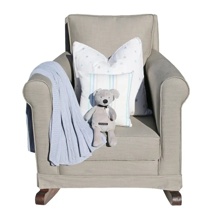 Tres Chic Rocking Chair in sand with dark oak rocking legs, styled with star and stripe scatter cushions, a grey teddy bear, and a soft blue throw for a warm and inviting nursery look.