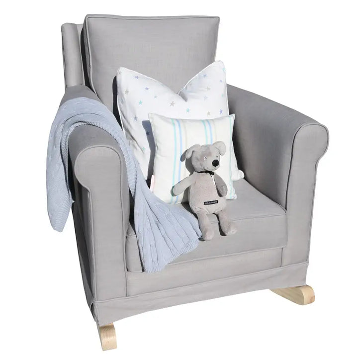 Tres Chic Rocking Chair in grey with natural oak rocking legs, styled with scatter cushions, a throw blanket, and a soft toy bear for a cozy nursery look.