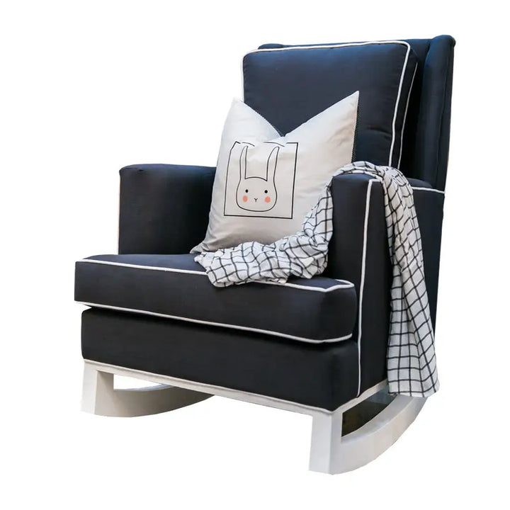 Peat Jayden rocking chair in dark charcoal fabric with contrasting white piping, styled with a playful bunny-print cushion and a checkered throw draped over the arm.
