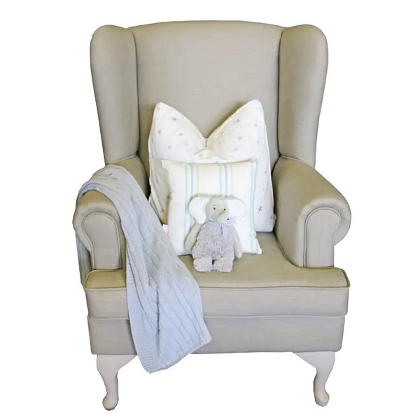 Oliver Feeding Chair in oatmeal fabric with classic wingback design, Queen Anne legs, and plush cushioning, styled with a grey knit blanket, star pillow, and soft elephant toy.
