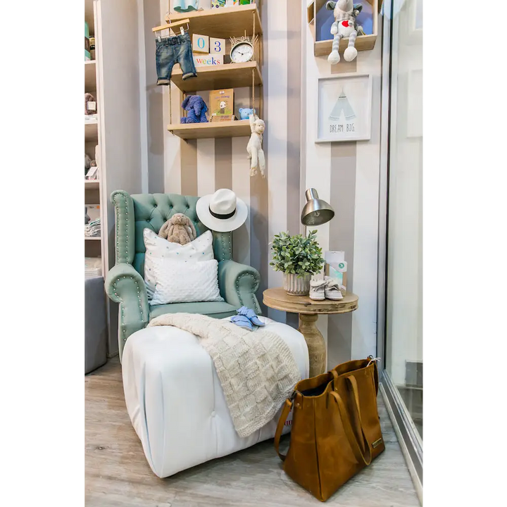 Sebastian Feeding Chair in green velvet upholstery, styled in a modern nursery with buttoned wingback design, studded arms, and Queen Anne legs, paired with a white ottoman and cosy décor.