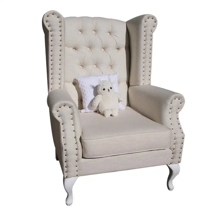 Sebastian Feeding Chair in cream fabric with diamond buttoned backrest, studded armrests, and Queen Anne legs, styled with a plush toy and cushion.