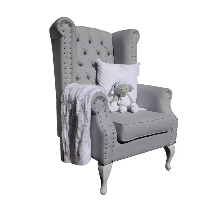 Sebastian Feeding Chair in grey fabric with diamond buttoning, studded armrests, and Queen Anne legs, styled with a white cushion, knit blanket, and soft toy.